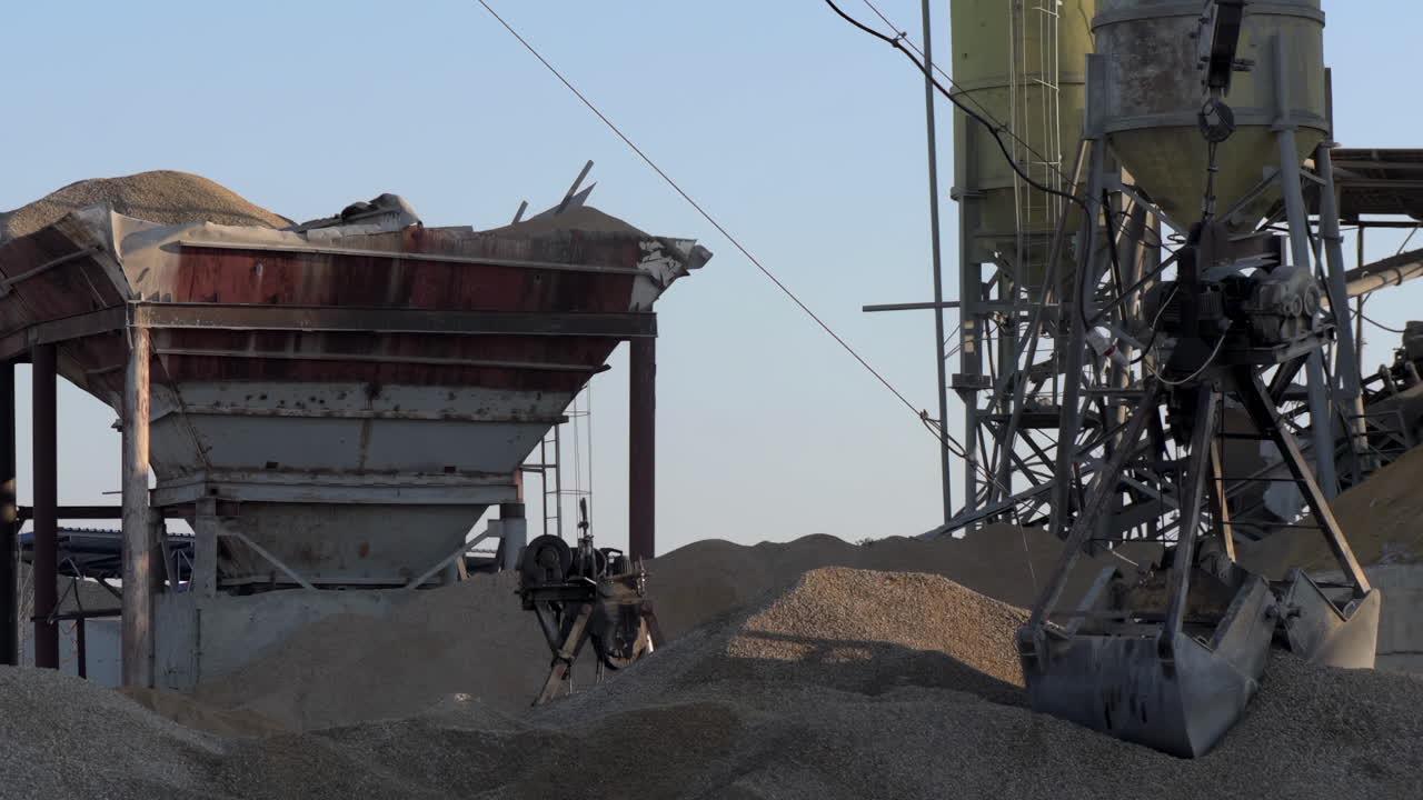 Un braccio meccanico sospeso a una gru che carica e trasporta cumuli di materiale granulare in un sito industriale