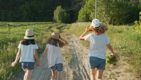 children three girls in hats holding hands running back along the rural country road