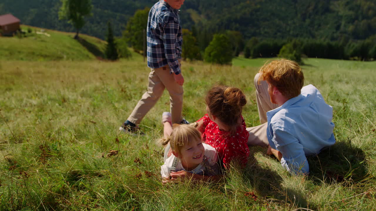행복한 가족이 휴식을 취하는 잔디 산 경사, 부모가 아이들과 함께 잔디 ⁇ 에 누워 있습니다.