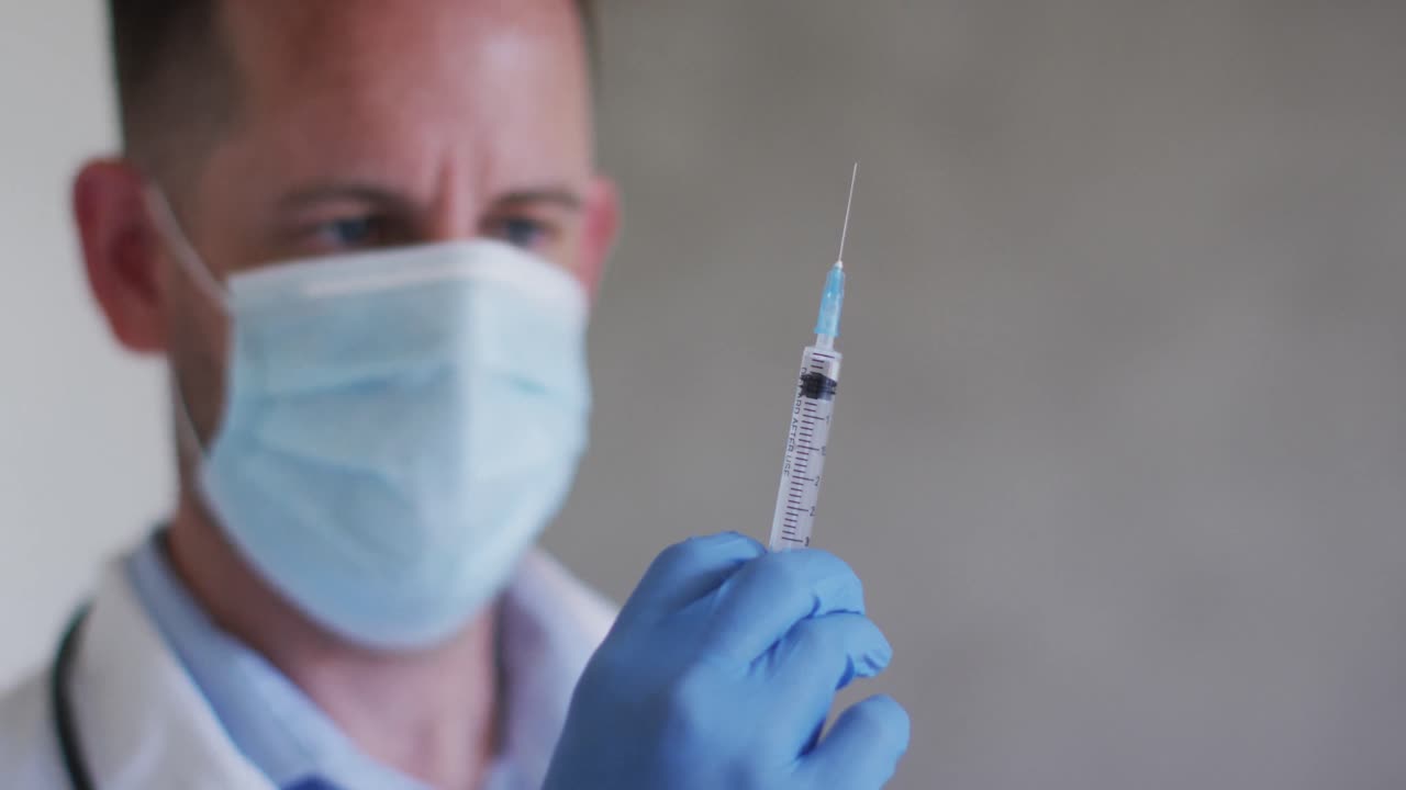 Portrait of caucasian male doctor wearing face mask and preparing vaccine