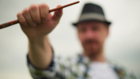 a painter, blurry except for his hand, holds a paintbrush aloft. the brush is in sharp focus, highlighting the moment of artistic engagement against a vague backdrop