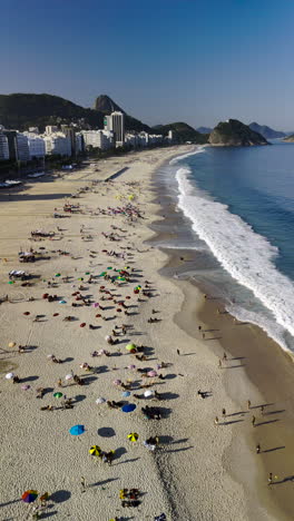 drone flying over copacabana beach rio de janeiro brazil, colorful umbrellas, people enjoying blue ocean, city skyscrapers, mountains background