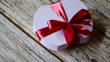 pink heart-shaped gift box with red ribbon on wooden table
