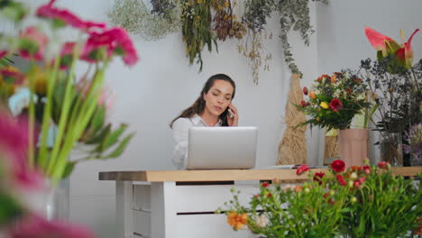 la mujer de negocios habla por teléfono móvil en la tienda de flores. el empresario trabaja en la computadora portátil en línea.
