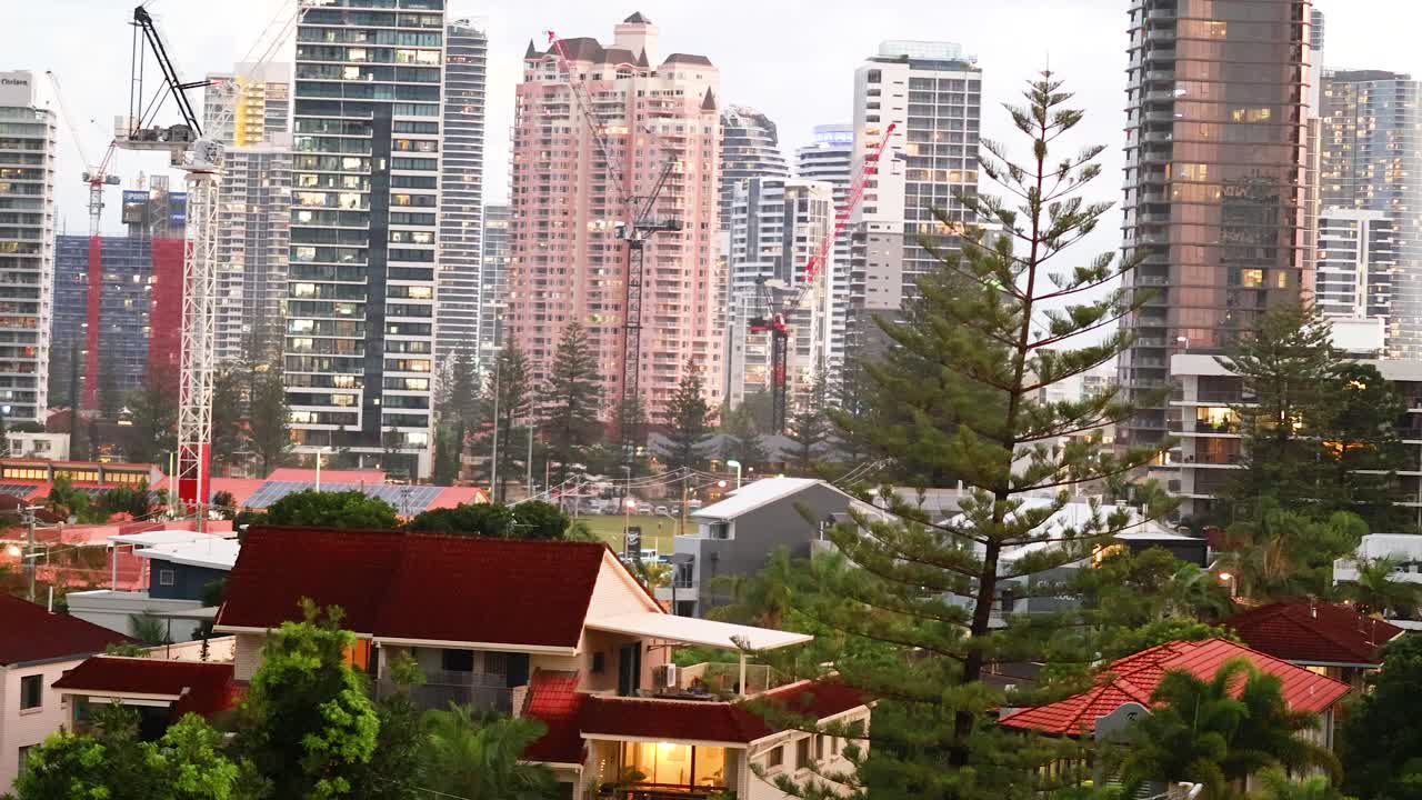 A panoramic view of Gold Coast's skyline with modern skyscrapers, cranes, and lush greenery under soft daylight