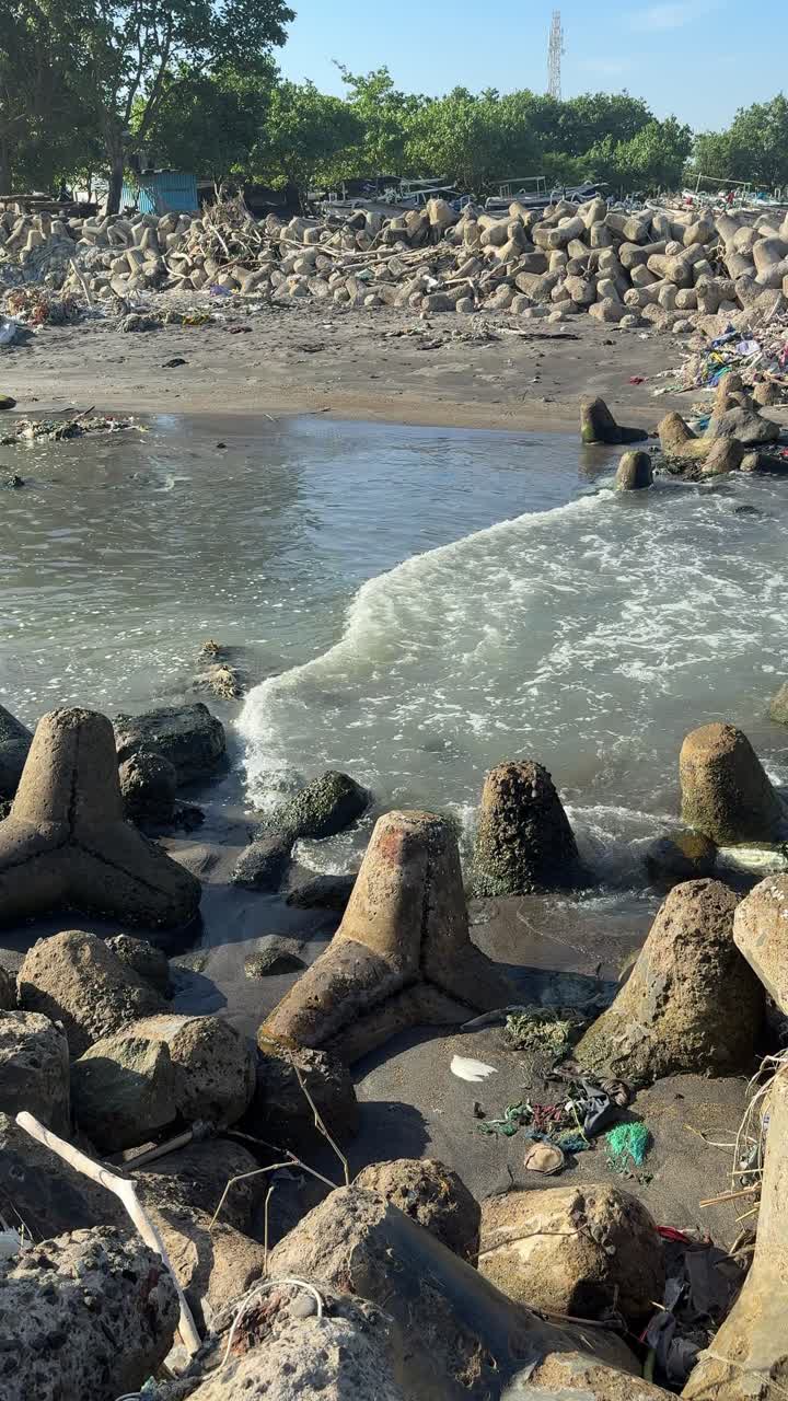 Onde oceaniche che si infrangono su una spiaggia inquinata con una barriera frangiflutti a tetrapodi.