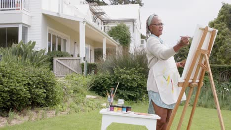 Senior-african-american-woman-painting-on-wooden-easel-in-garden,-slow-motion