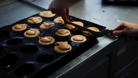 Medium-close-up-shot-of-baker-scrapping-excess-batter-mix-from-a-cupcake-tray