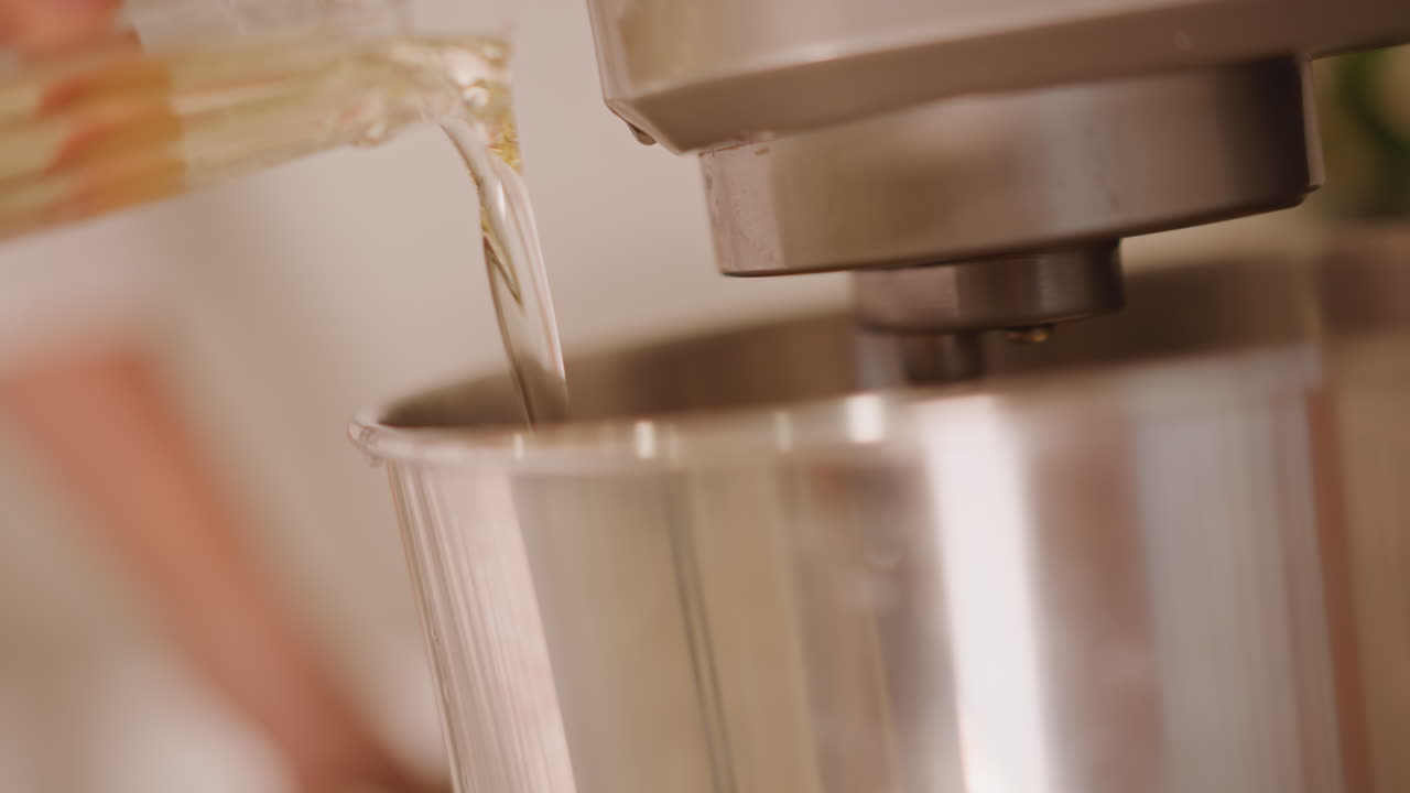 Una cottura accogliente con un mix di zucca. Primo piano di un fornaio che versa olio in una ciotola durante una sessione di preparazione autunnale. L'atmosfera calda mostra il fornaio versare l'olio nella ciotola mentre l'impasto per la torta di zucca inizia a prendere forma.