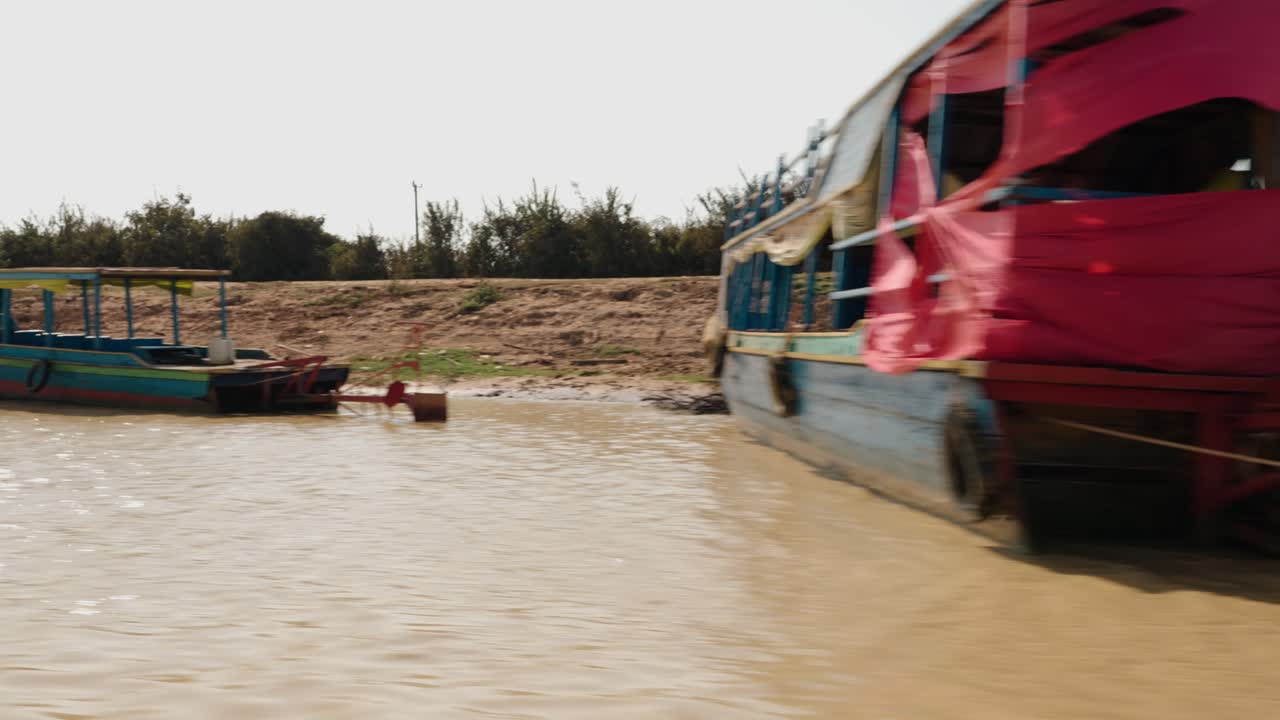 moving shot of a wooden riverboat along muddy shoreline near Tonle Sap lake