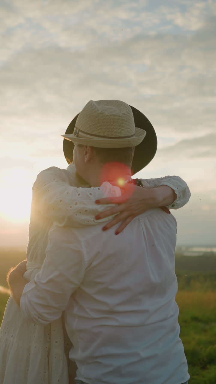 해가 지는 동안 두 연인이 잔디에서 따뜻하게 안고, 둘 다  옷과 모자를 입고, 가는 해의 황금빛은 로맨틱한 분위기를 향상시니다.