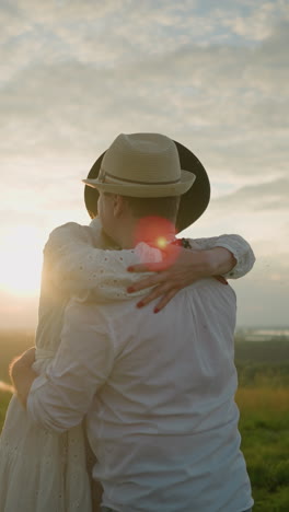 dos amantes se abrazan cálidamente en un campo cubierto de hierba al atardecer, ambos con trajes y sombreros blancos. la luz dorada del sol que se pone mejora la atmósfera romántica mientras se abrazan estrechamente