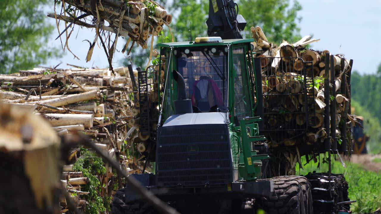 A bokeh shot capturing forest machinery in slowmo as it unloads cut wood from a trailer to the ground. The blurred background enhances the focus on the machinery, creating a dynamic, cinematic scene.