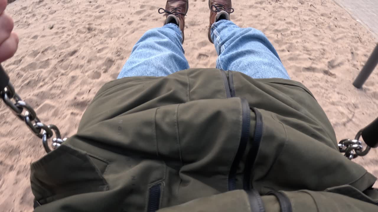 Young adult having fun on swings in cold weather, POV