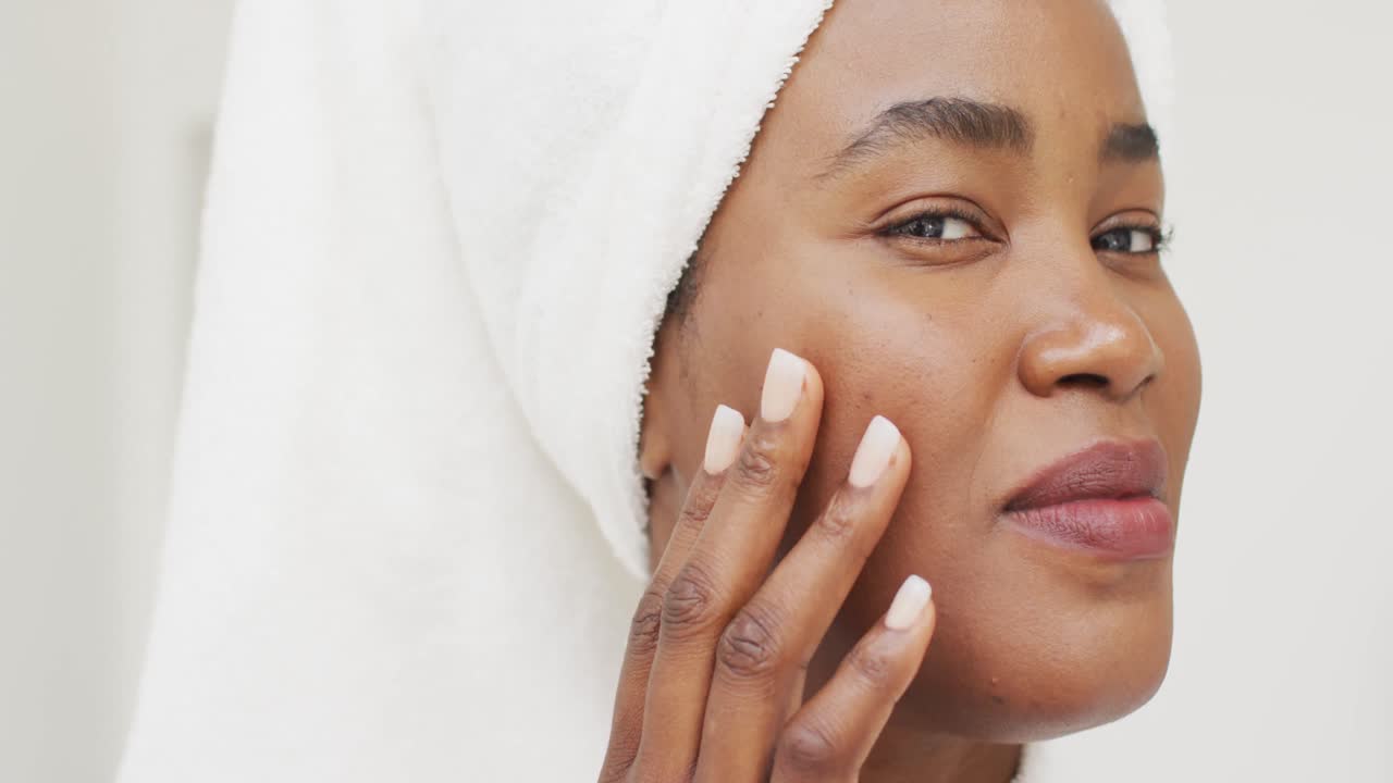 Video of happy african american woman in robe moisturizing face