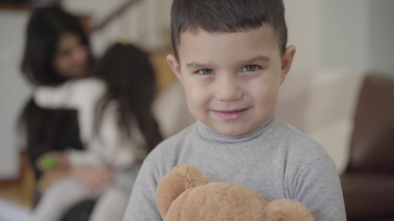 Close-up face of a charming Middle Eastern grey-eyed boy with dark hair holding the teddy bear and looking at the camera