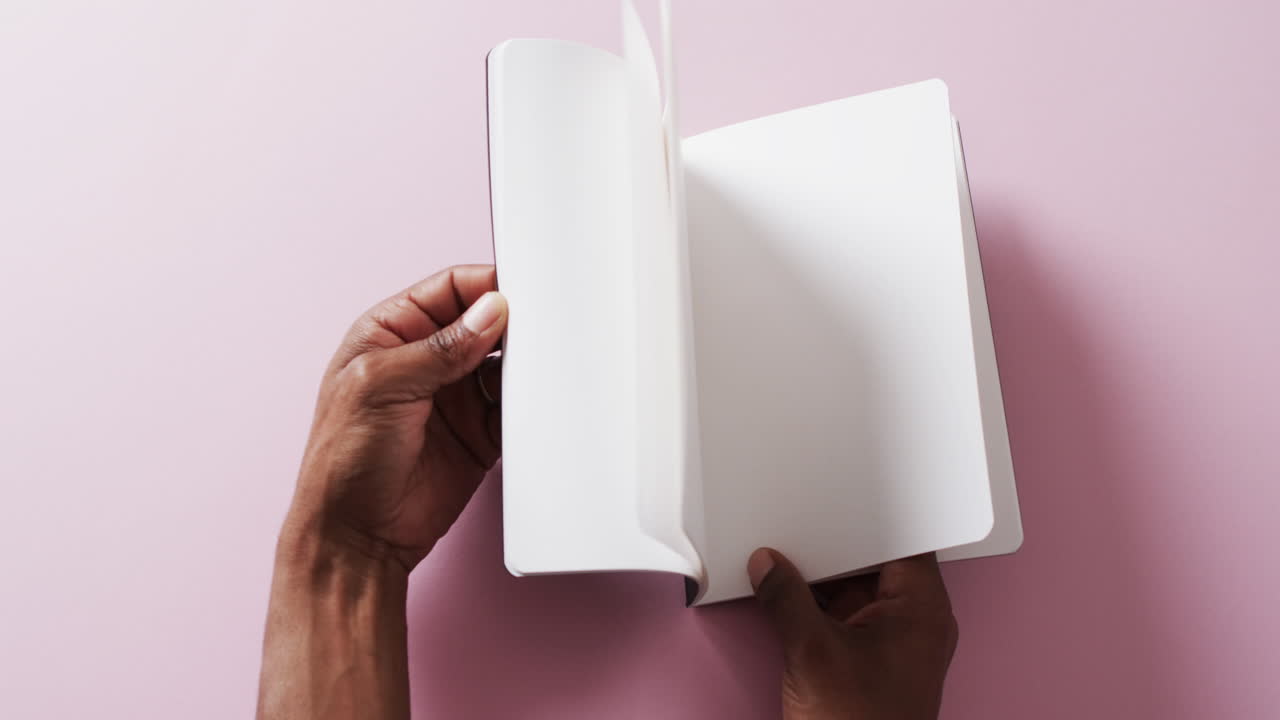Close up of hand leafing through book with copy space on pink background in slow motion