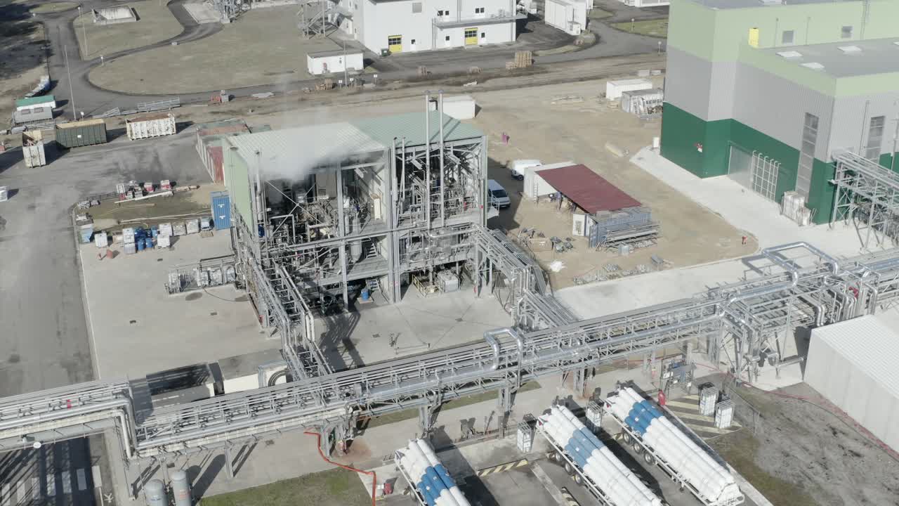 Drone orbiting view over industrial processing unit with steam, revealing extensive piping network and nearby tanker trucks, Castets, France
