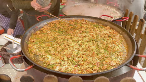 Water-being-added-to-chicken-and-vegetable-paella-in-a-large-frying-pan-in-an-Edinburgh-street-market,-Edinburgh,-Lothian,-UK