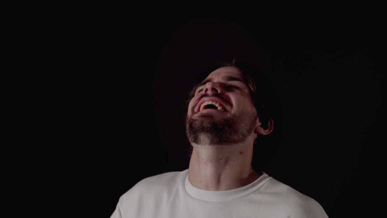 Giovane uomo alla moda che ride e sorride, gesto felice, primo piano, sfondo nero.