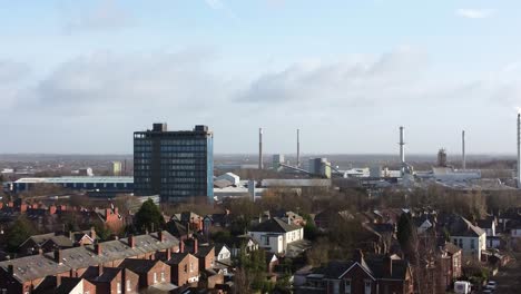 Aerial-view-over-park-trees-to-Merseyside-industrial-townscape-with-blue-skyscraper,-Merseyside,-England