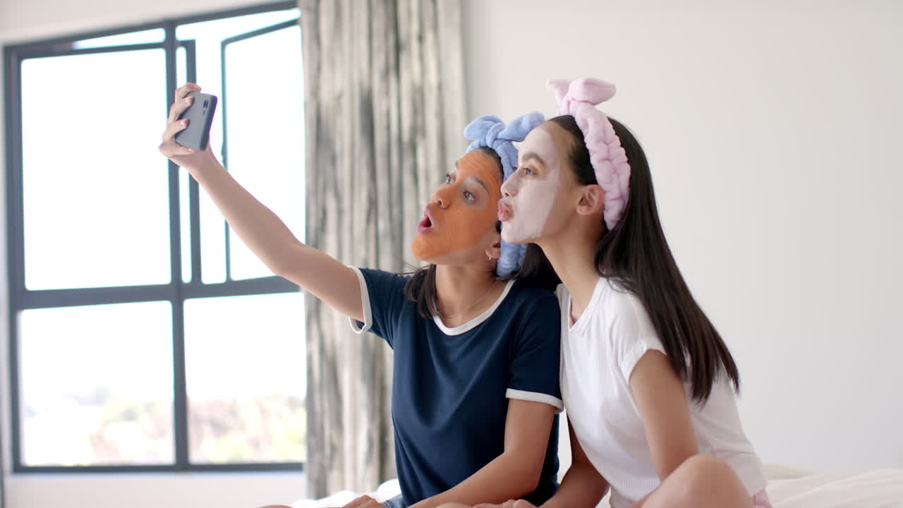 Two biracial teenage girl friends are taking selfie, making funny faces at home