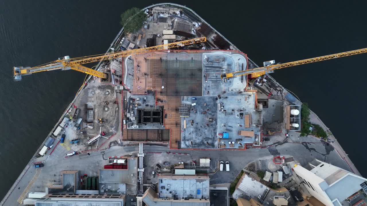 Yellow cranes of large construction site during building phase at bayshore of Tampa. Aerial ascending top down. Framing of skyscraper tower.