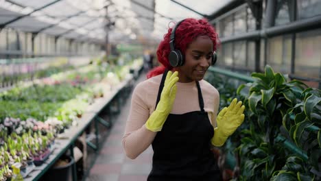 Biracial-woman-enjoying-work-in-greenhouse,-dancing---florist-holding-pot