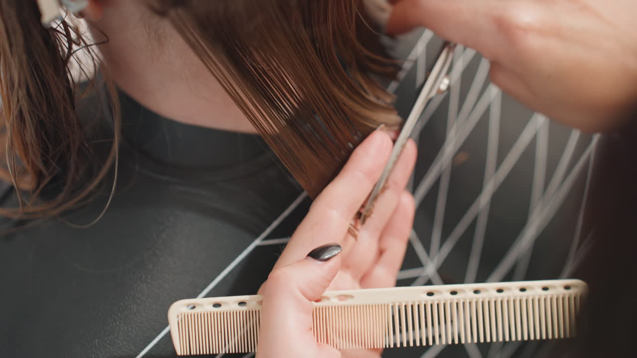 closeup stylist trimming wet hair with comb and shears, assistant holding section, intimate salon atmosphere with glossy strands, detailed manicure hands guiding cut for precise texture and finish