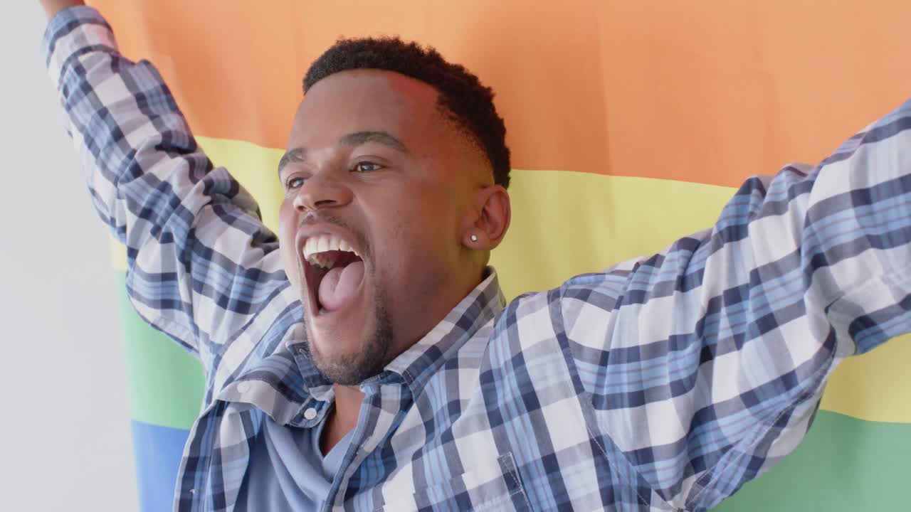 hombre afroamericano feliz sosteniendo la bandera del arco iris lgbt y sonriendo, cámara lenta