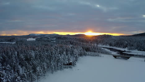 aerial view across glowing sunrise snow covered mountains over woodland trees and ice lake bridge