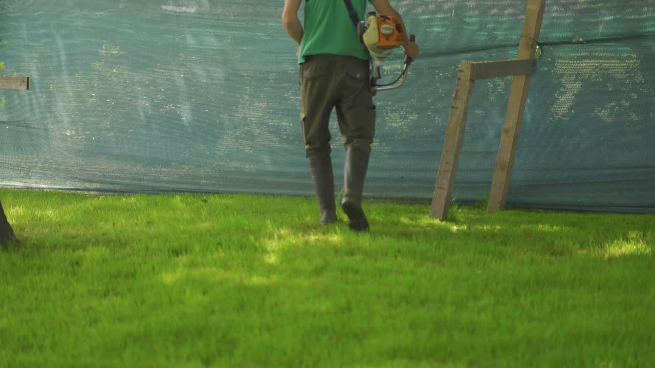 정원에서 크러시 커터로 잔디를 자르는 남성 노동자의 추적 샷, 중간 샷