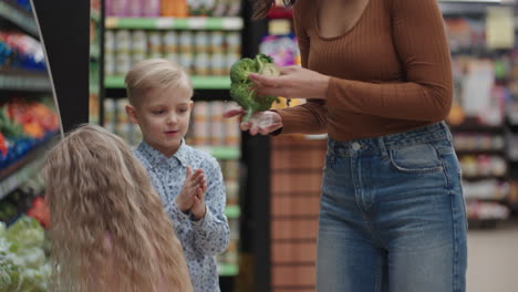 a mother in a protective mask with two children is buying groceries at the supermarket. buying food vegetables and fruits with children