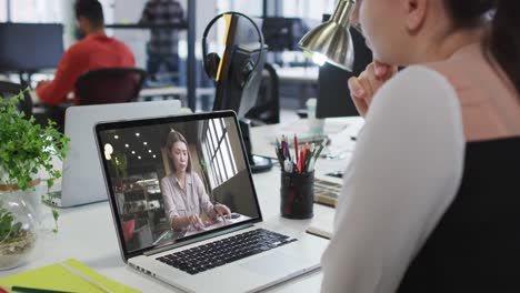 Caucasian-woman-having-a-video-call-on-laptop-with-female-colleague-at-office