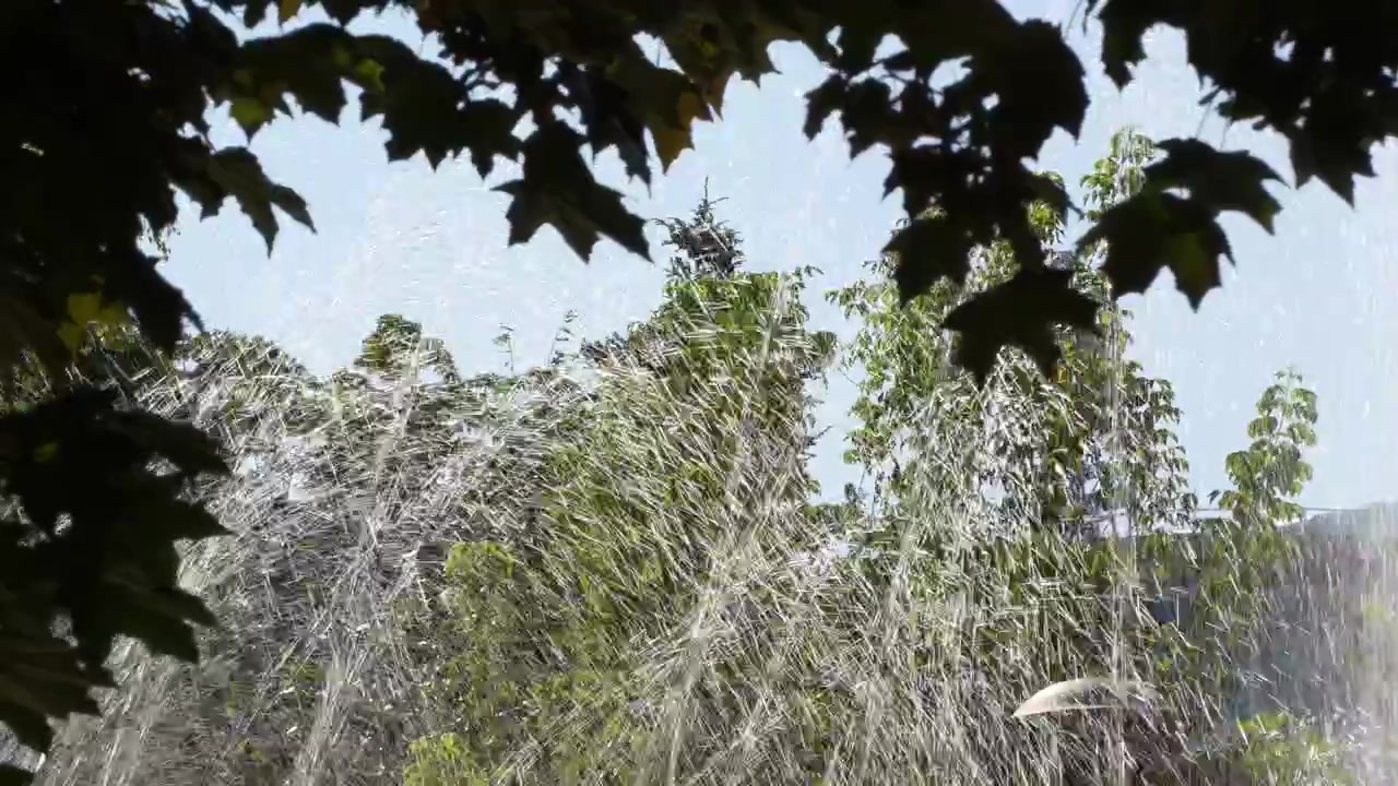 Fountains water droplets with park background of green trees in morning sunshine