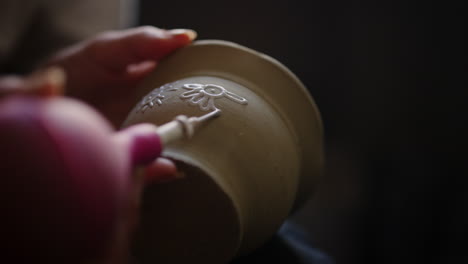 female craftmaster decorated clay pot in pottery. unknown woman drawing on pot