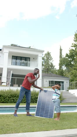 vertical video: father and son holding solar panel, discussing installation near pool in backyard