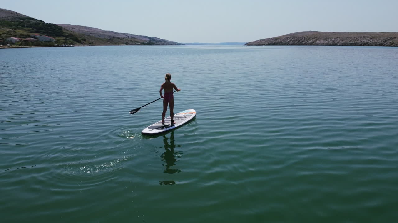 크로아티아 파그 섬의 아드리아 해에서 노를 젓는 소녀의 실루엣과 함께 화창한 여름날의 공중 풍경