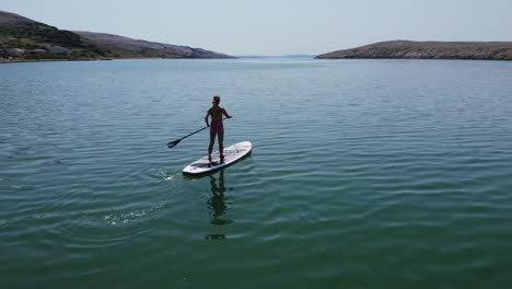 Paisaje-Aéreo-De-Un-Día-Soleado-De-Verano-Con-La-Silueta-De-Una-Niña-Remando-En-El-Mar-Adriático-De-La-Isla-De-Pag-En-Croacia