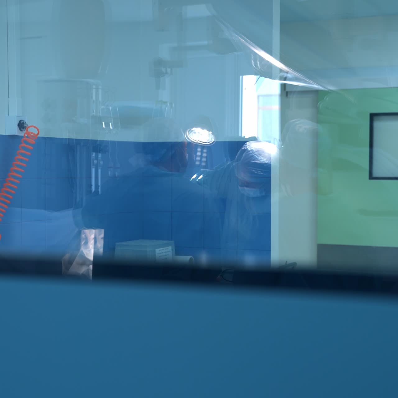 Window in operating room reflecting the surgeons performing operation. Doctors busy at their work