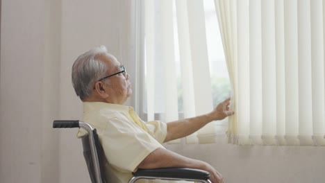 old asian man sits in a wheelchair and looks out the window. health care and insurance, retirement concept