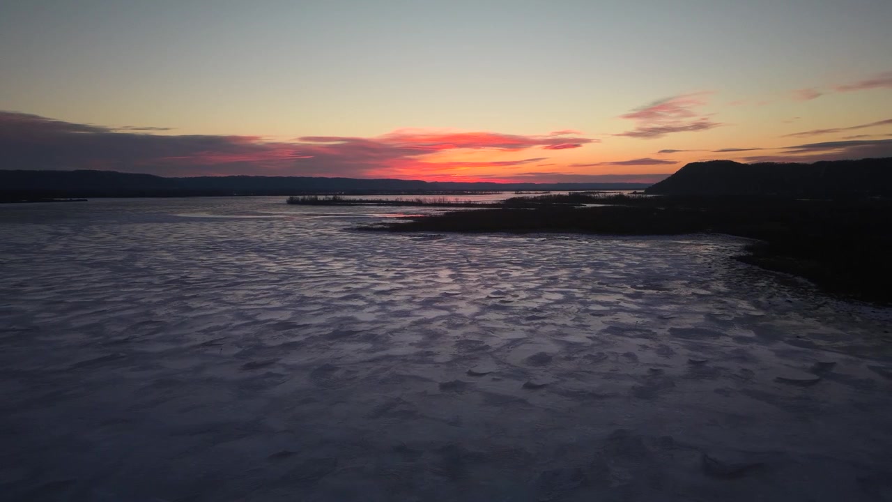 Vista aerea con drone del Loch Morlich ghiacciato al tramonto nel Parco Nazionale di Cairngorms, che mostra ghiaccio strutturato, acqua calma e un cielo serale colorato sul paesaggio delle Highlands.