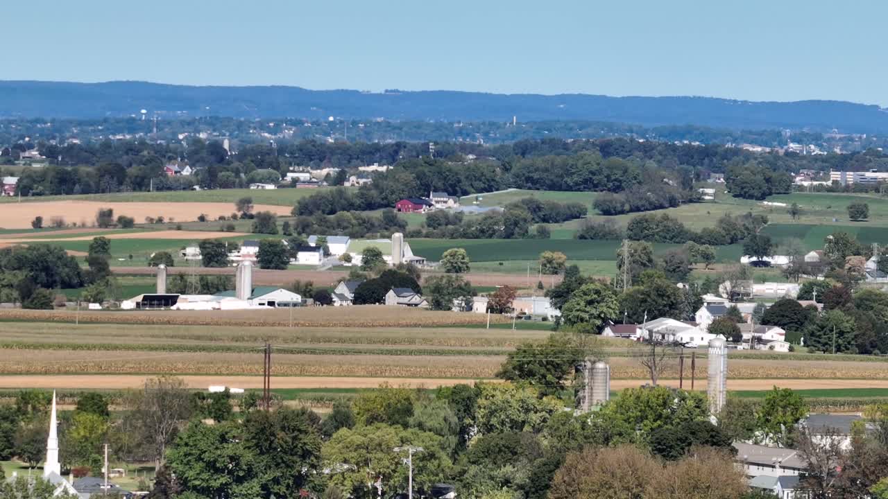 Aerial wide shot of peaceful american countryside with farmland fields and farmsteads. Mountains and colored trees in fall season. Silo storage of farmsteads in United States