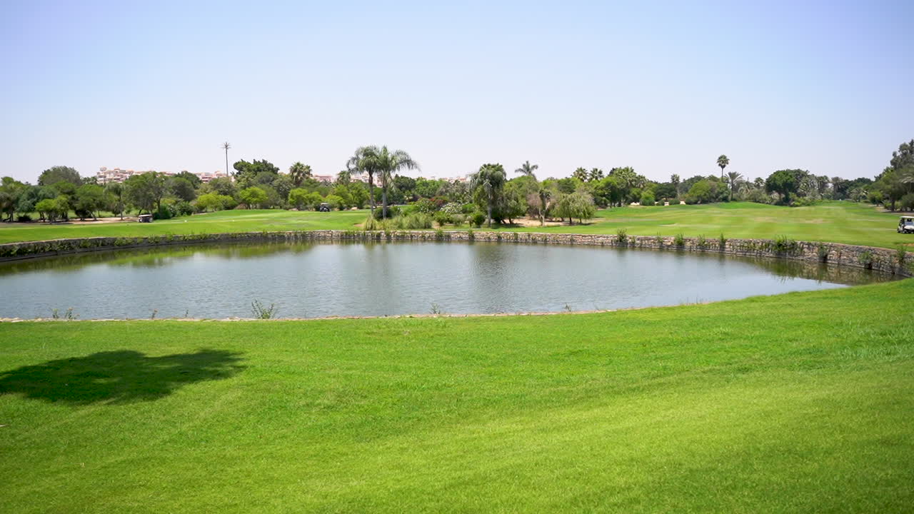 un hermoso campo de golf con césped verde, árboles, lago y césped de plumas en un día soleado