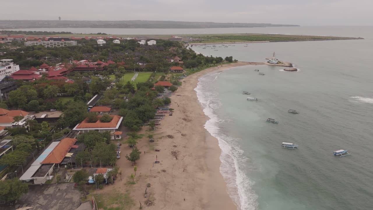 Aerial View of Pantai Jerman, Bali – Waves Crash on the Shore, Boats Rest Along the Coast, and a Stunning Resort Overlooks the Beach.