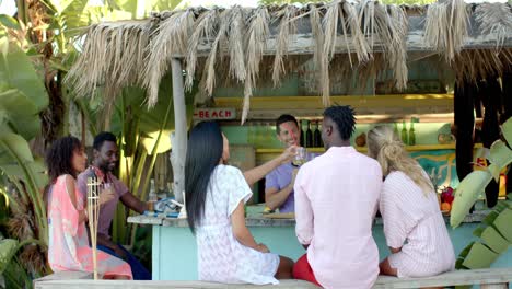 happy diverse group of friends talking and drinking cocktails at beach bar