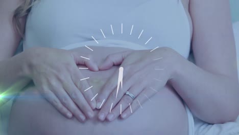 Clock-with-fast-moving-hands-over-happy-pregnant-caucasian-woman-making-heart-hands-on-belly