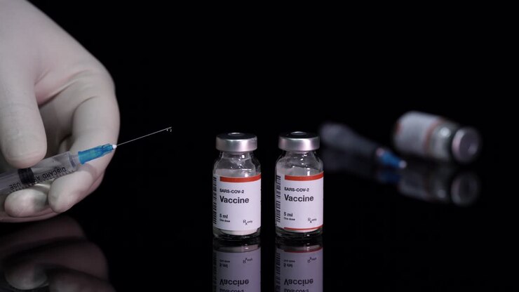 Covid-19 vaccine bottles and hand holds a filled syringe treating Coronavirus pandemic