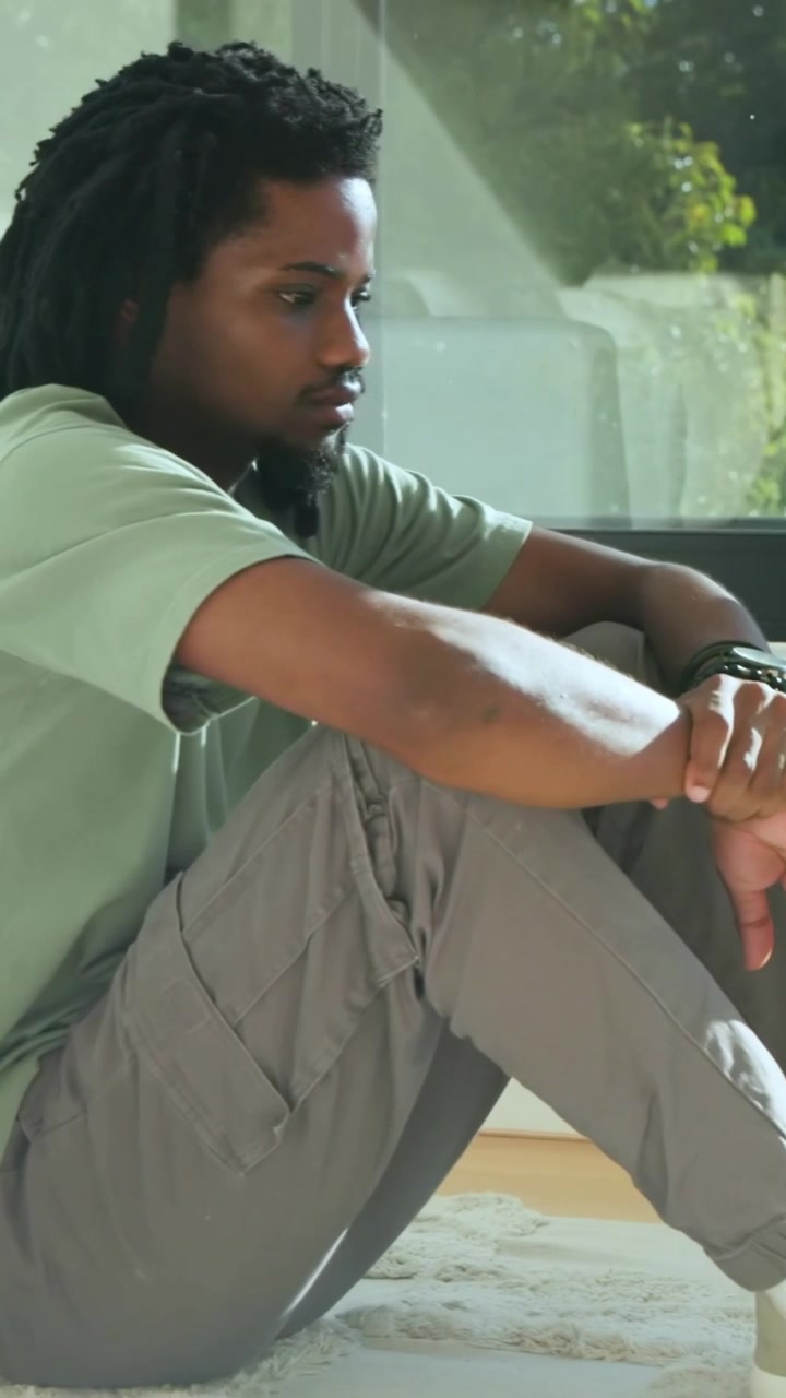Vertical video: Camera zooming man in green tee shifting gaze at home by window to look outside