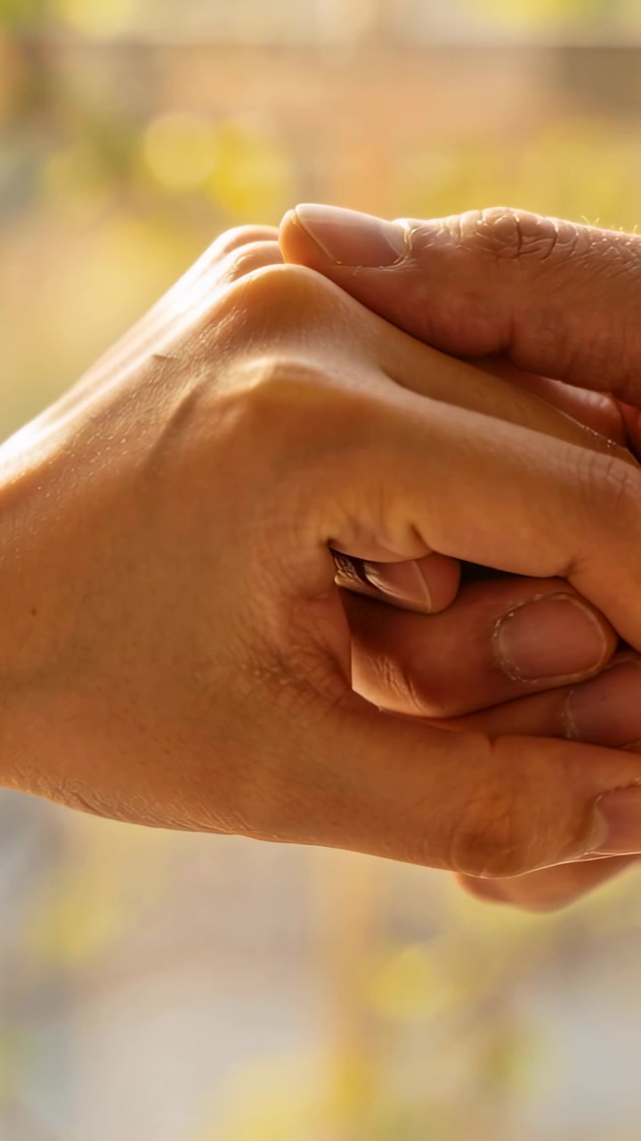 Vertical video: Reaching, one adult hand clasping another by sunny window, soothing, showing band
